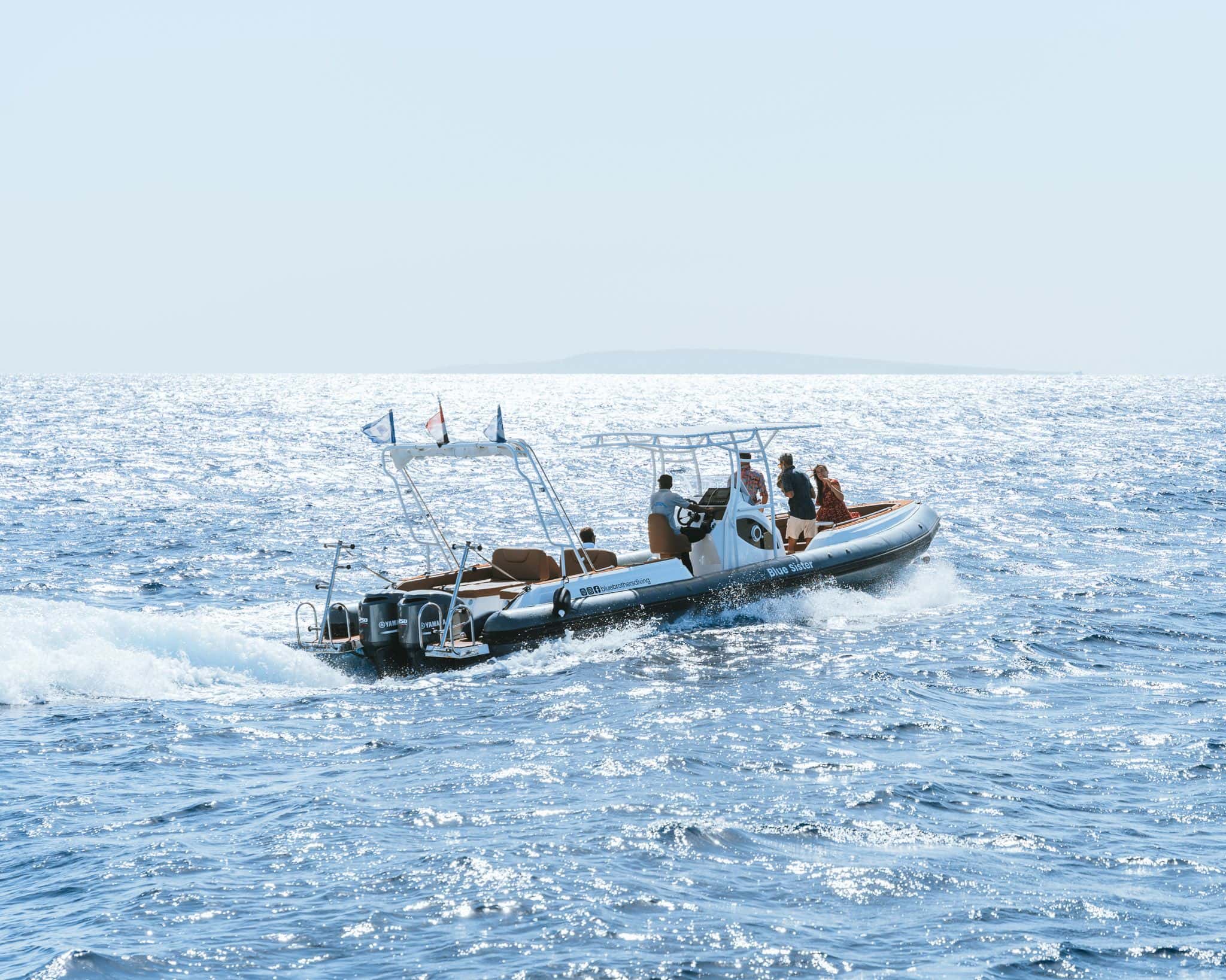 A black and white rigid inflatable boat (RIB) with several people speeding across choppy blue water.