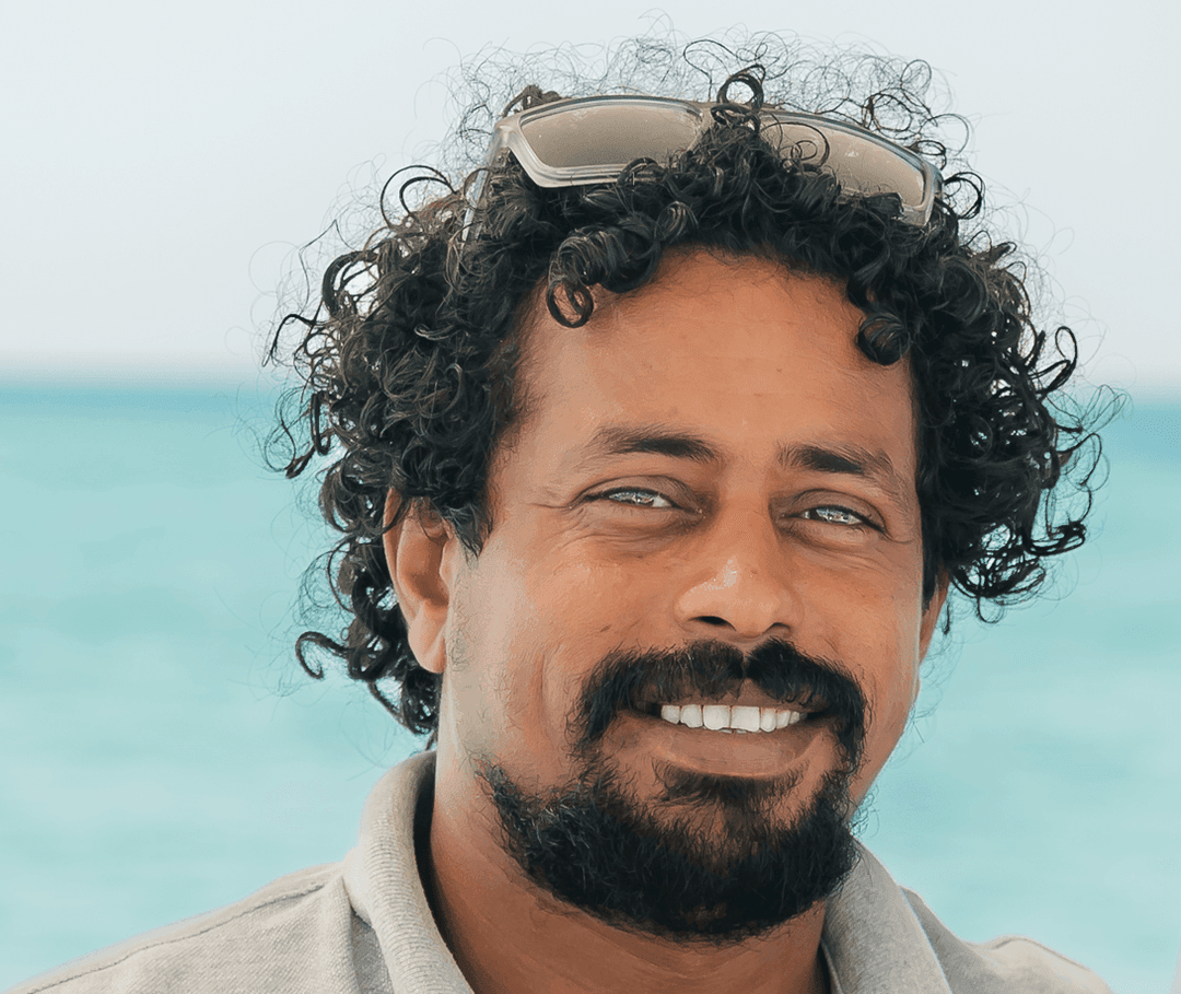 Smiling man with curly dark hair, beard, and sunglasses on his head.