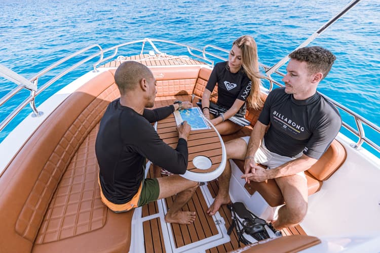 Three people chatting around a wooden table on a small boat, enjoying the sunny day.