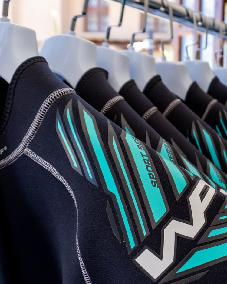 Row of black and turquoise wetsuits hanging neatly on a retail display rack.