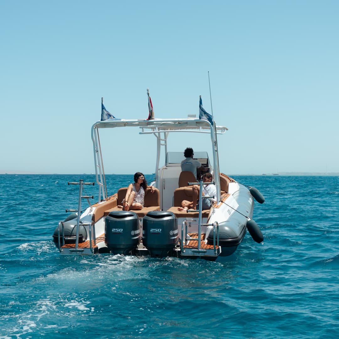 A boat with people on board sails away on the vast expanse of blue sea.