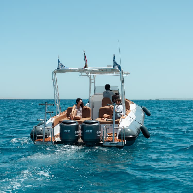 A boat with people on board sails away on the vast expanse of blue sea.