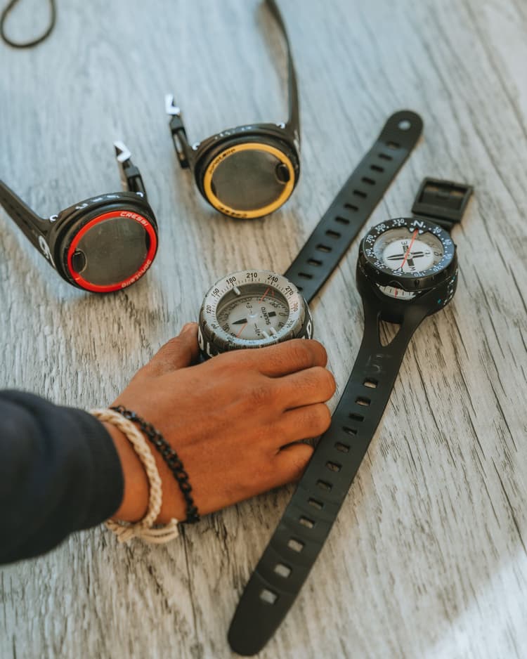 A diver's hand holds a black dive computer with two others nearby.