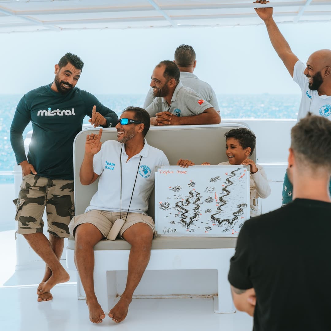 A group of people sitting on a boat, one holding a whiteboard with a map.