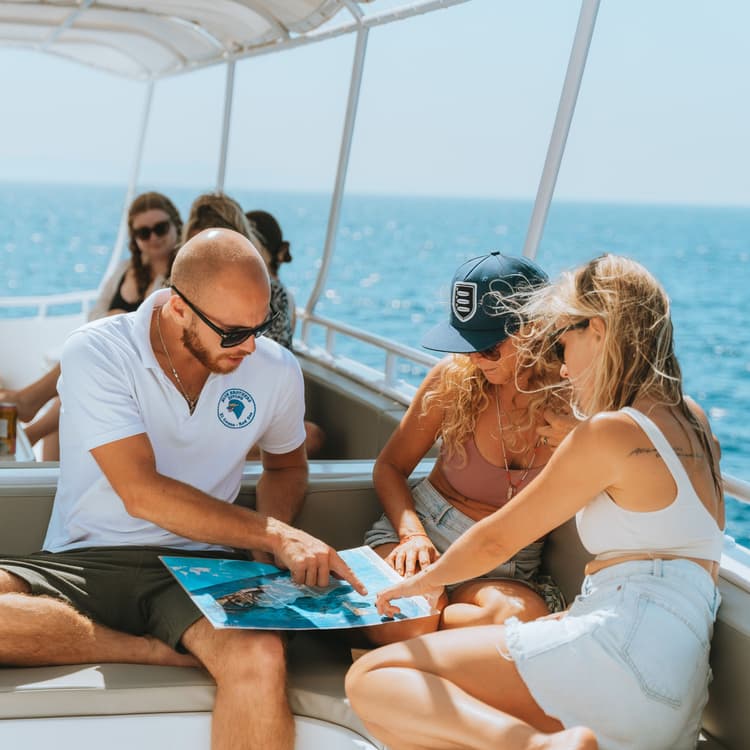 Boat guide points to a map for a woman on a sunny ocean tour.