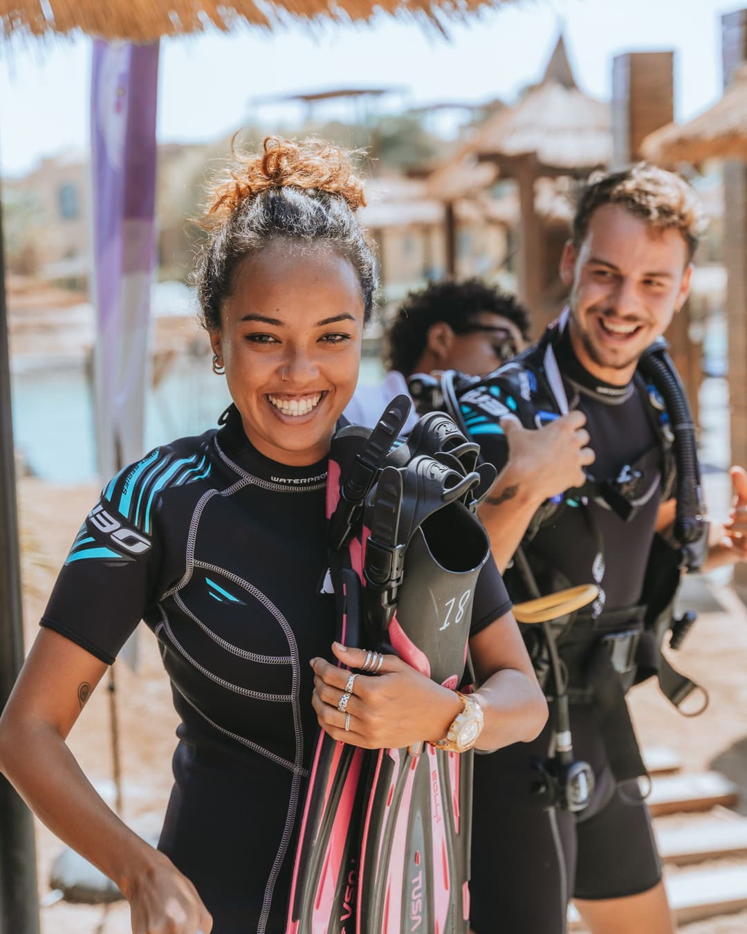 A smiling man and woman in wetsuits, holding masks and fins, ready for their dive.