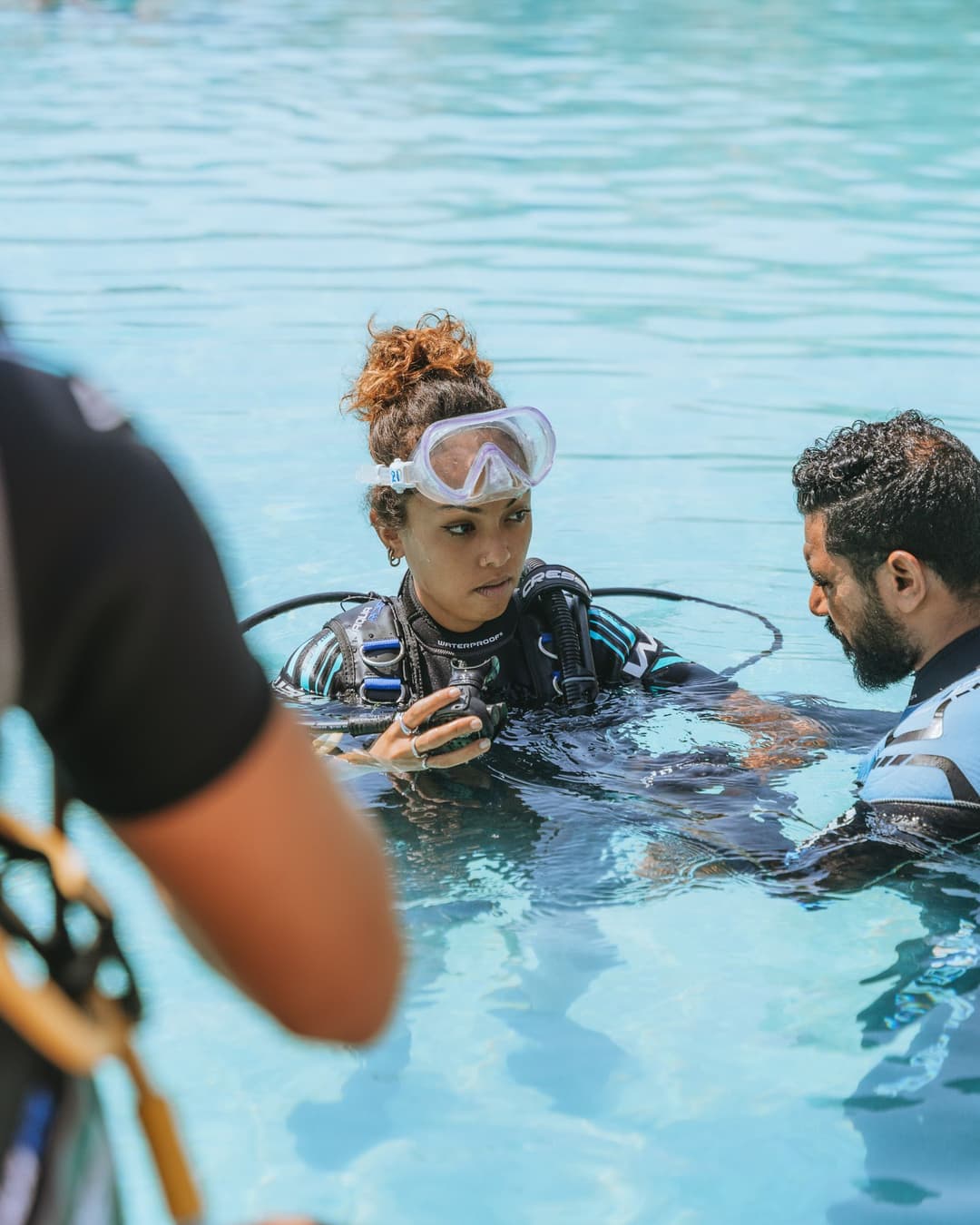 A woman in a wetsuit and dive mask receiving instruction from a man in a swimming pool.