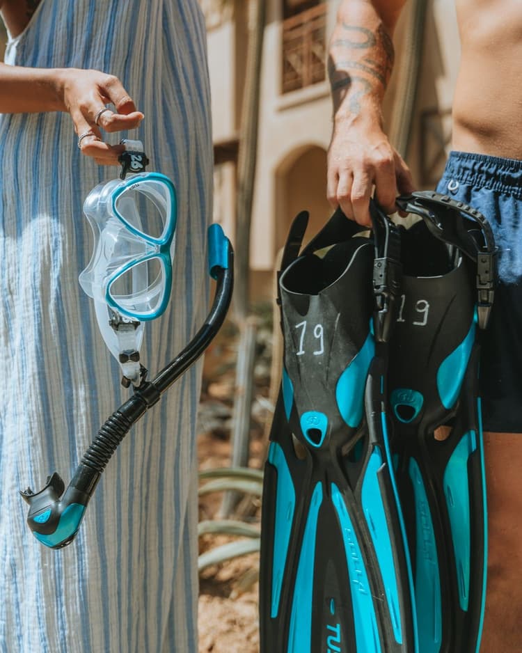 Two people holding blue and black snorkeling gear, including a mask, snorkel, and fins.