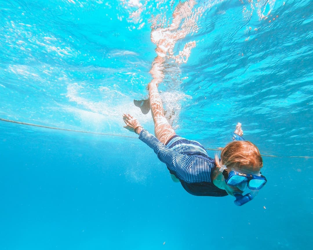 Child in snorkel mask and wetsuit swims underwater.