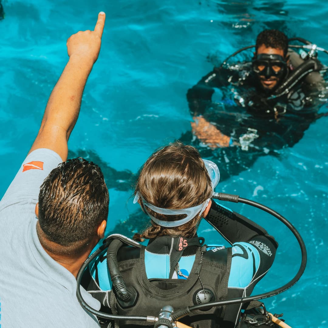 Two divers in a swimming pool, one being instructed by another pointing gesture.