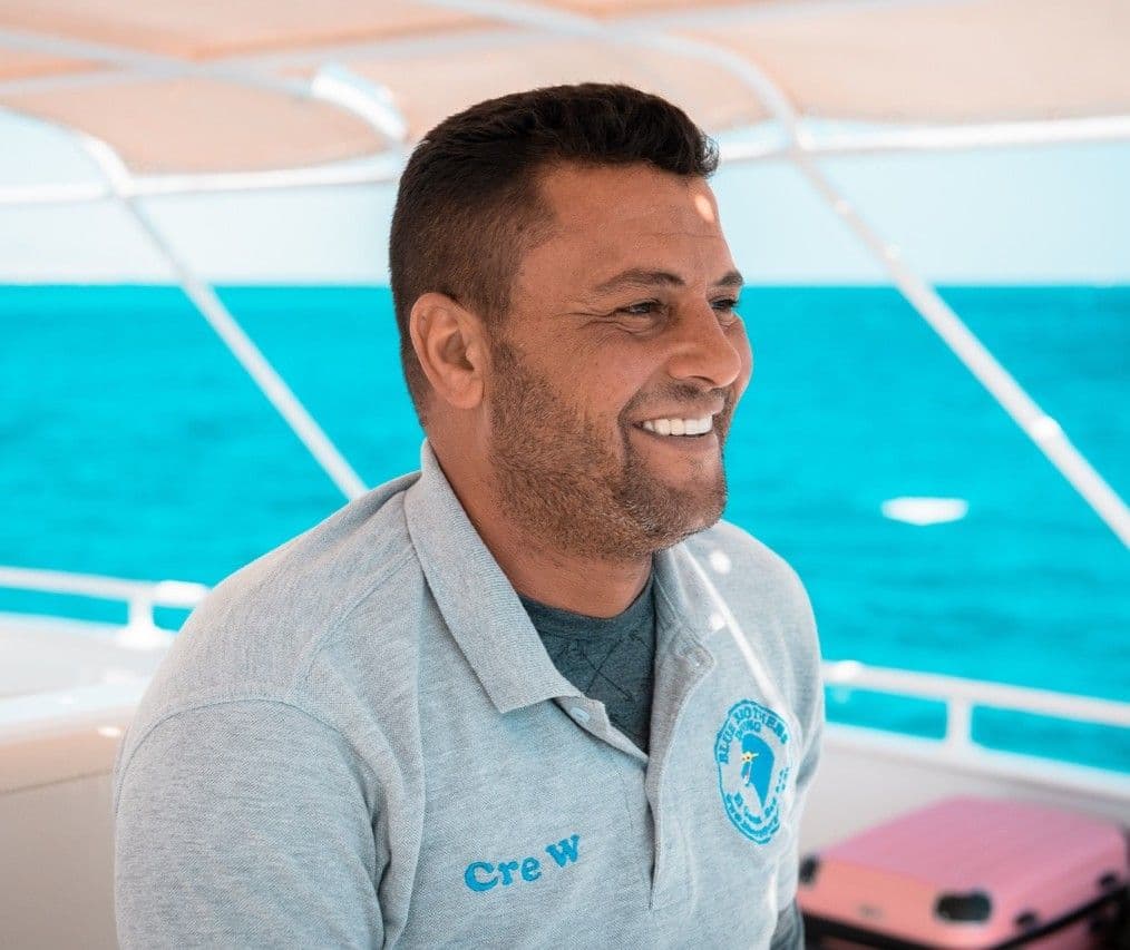Smiling man in a grey 'Crew' polo shirt on a boat, looking happy.