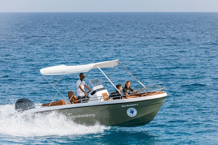 A small motorboat with three people speeding across the blue ocean water, creating a wake.