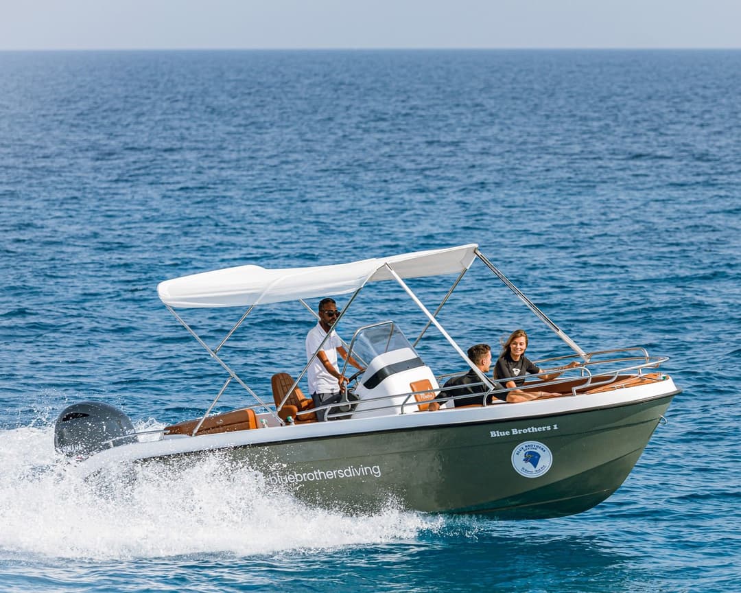 A motorboat with three people cruises on clear blue water under a bright sky.