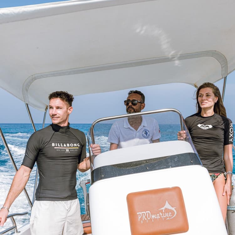 Three people enjoy a sunny day on a boat, one steering through blue ocean.