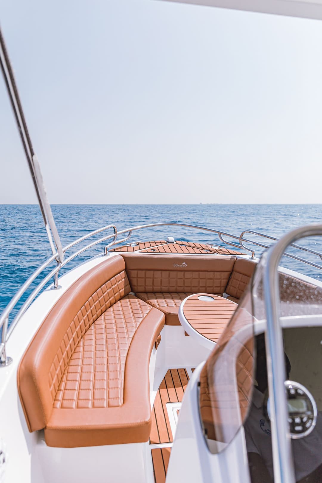 Empty front deck of a small motorboat featuring comfortable brown wooden seating and railing.