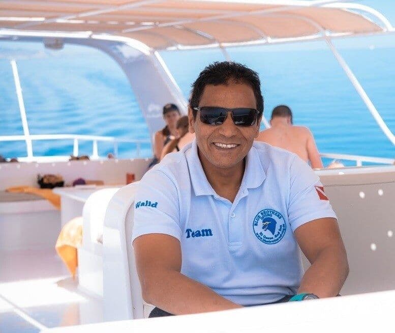 Smiling man, Tuan, wearing sunglasses and a blue polo shirt while relaxing on a boat.